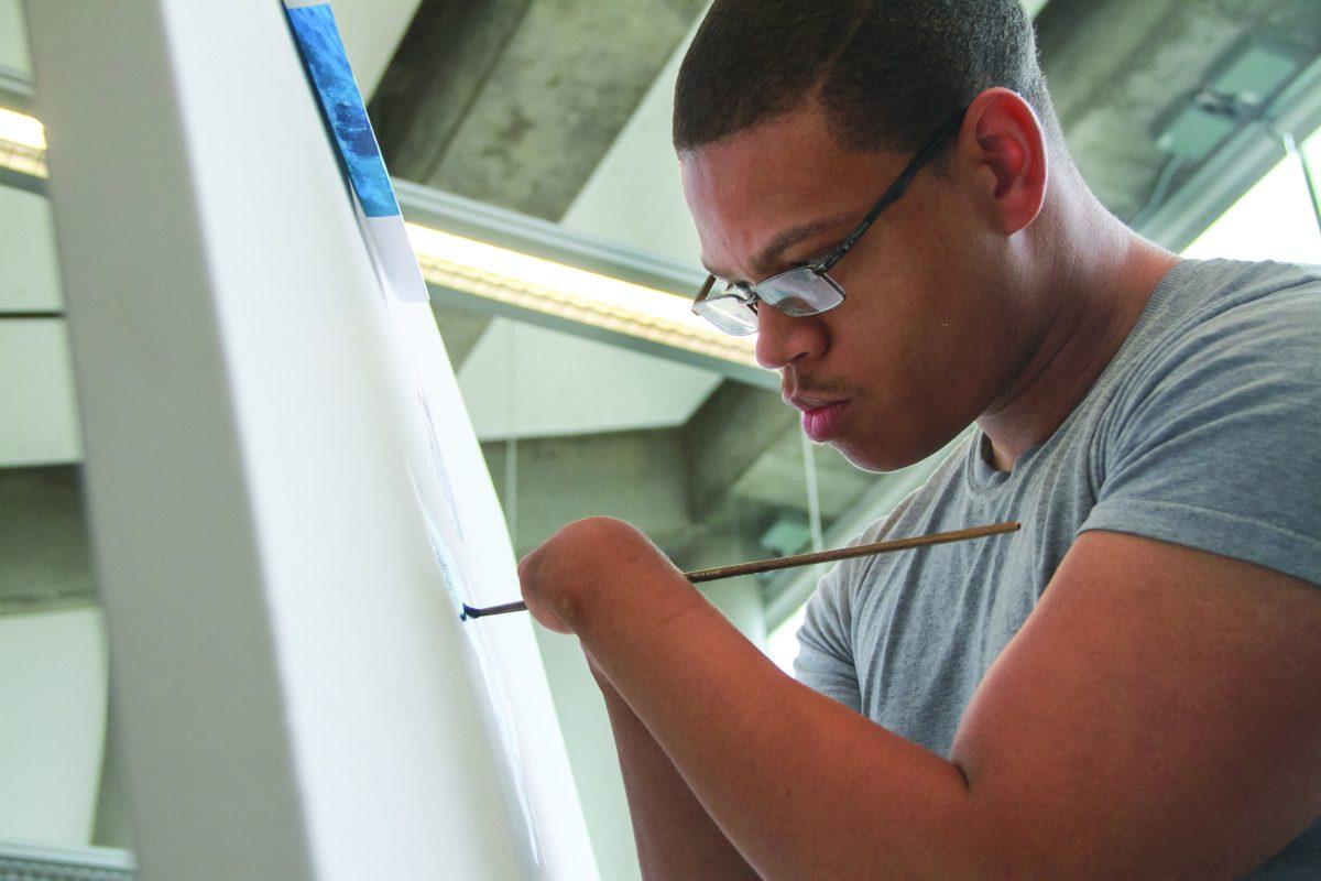 Concentrating on the canvas, alumnus Desmond Blair pursues his passion for art. Even though Blair was born without hands, he challenged himself and was later accepted to the ATEC program at UTD. Photo by Saher Aqeel | Photo Editor.