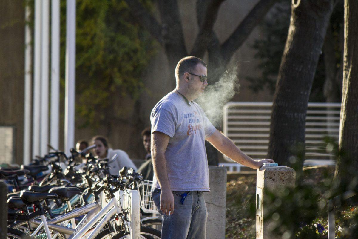 Jason Heard, a student from UT Arlington, smokes outside the McDermott Library. Heard said he studies at the library every weekend and was unaware of the smoking ban. Photo by Michael Stout | Mercury Staff.